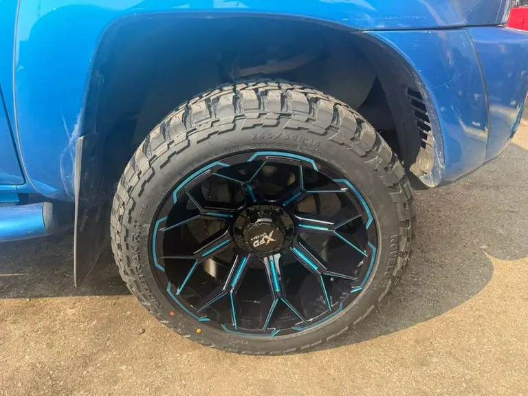 Close view of a blue truck's tire marked 265/50R20 and black wheel with blue accents