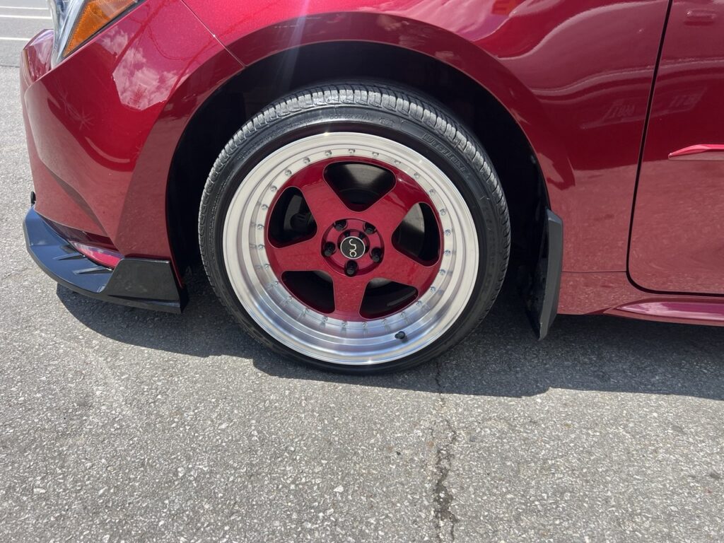 Close-up view of a deep-dish red custom rim with polished lip on the front axle.
