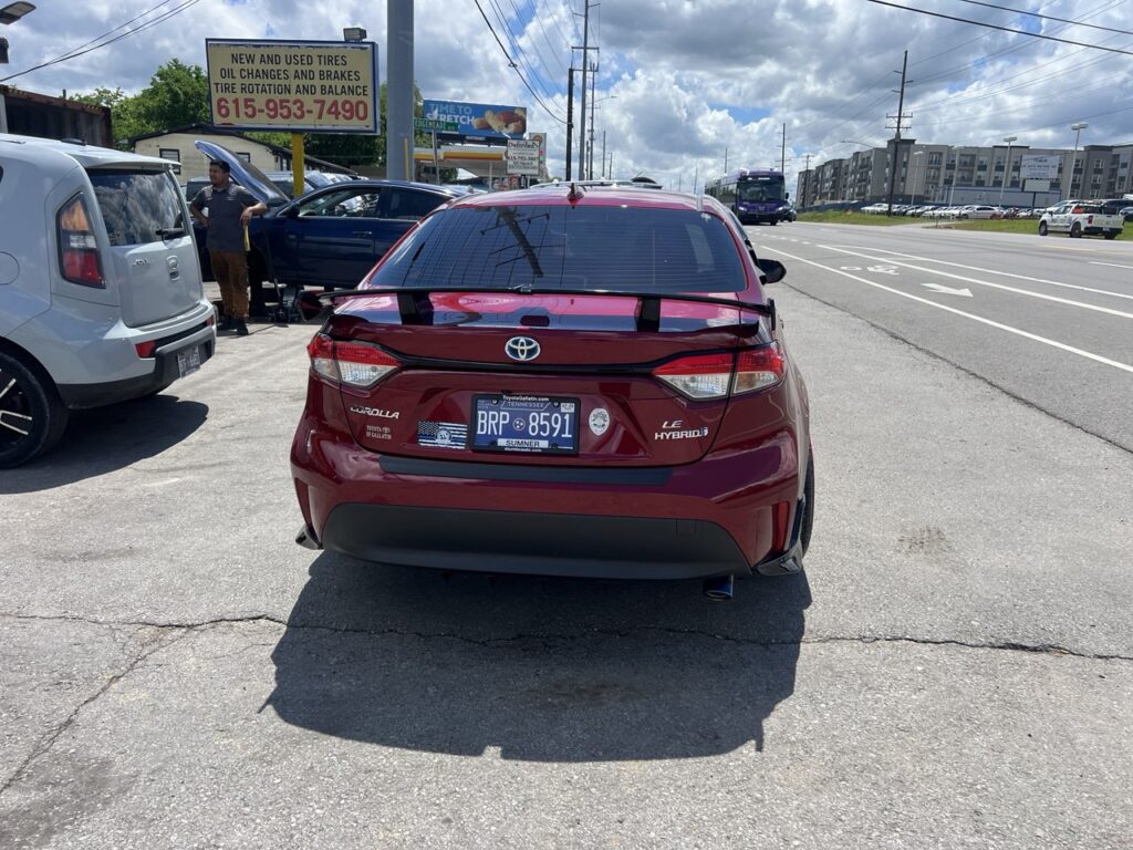 Rear view of a 2021 Toyota Corolla LE Hybrid with spoiler, aftermarket exhaust tip, and Tennessee plates.