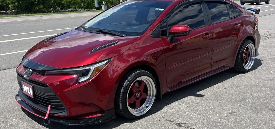Angled front-side view of a red Toyota Corolla with aftermarket wheels and aerodynamic body kit.